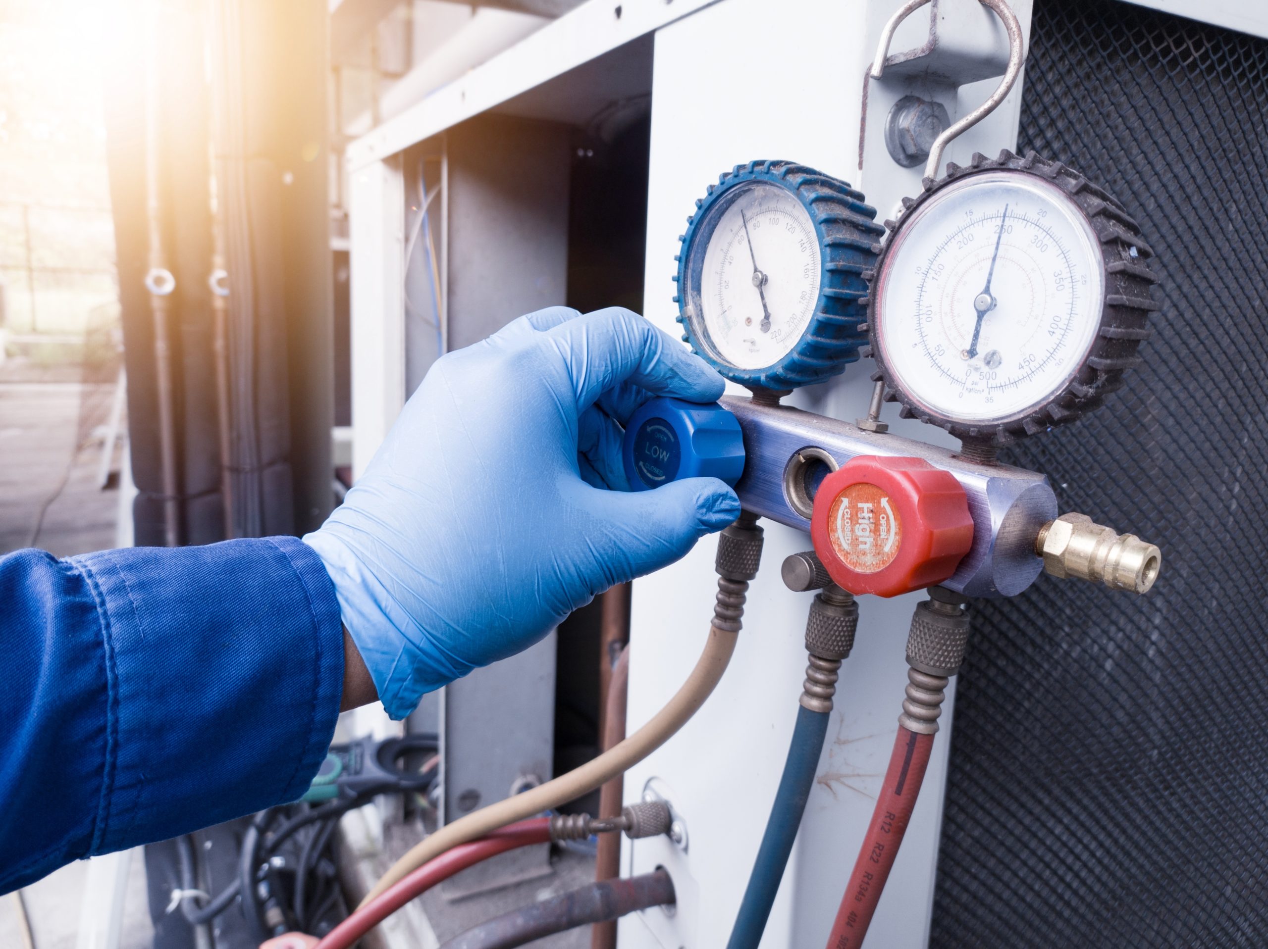 Technician adjusting HVAC system pressure gauges with blue gloved hand.